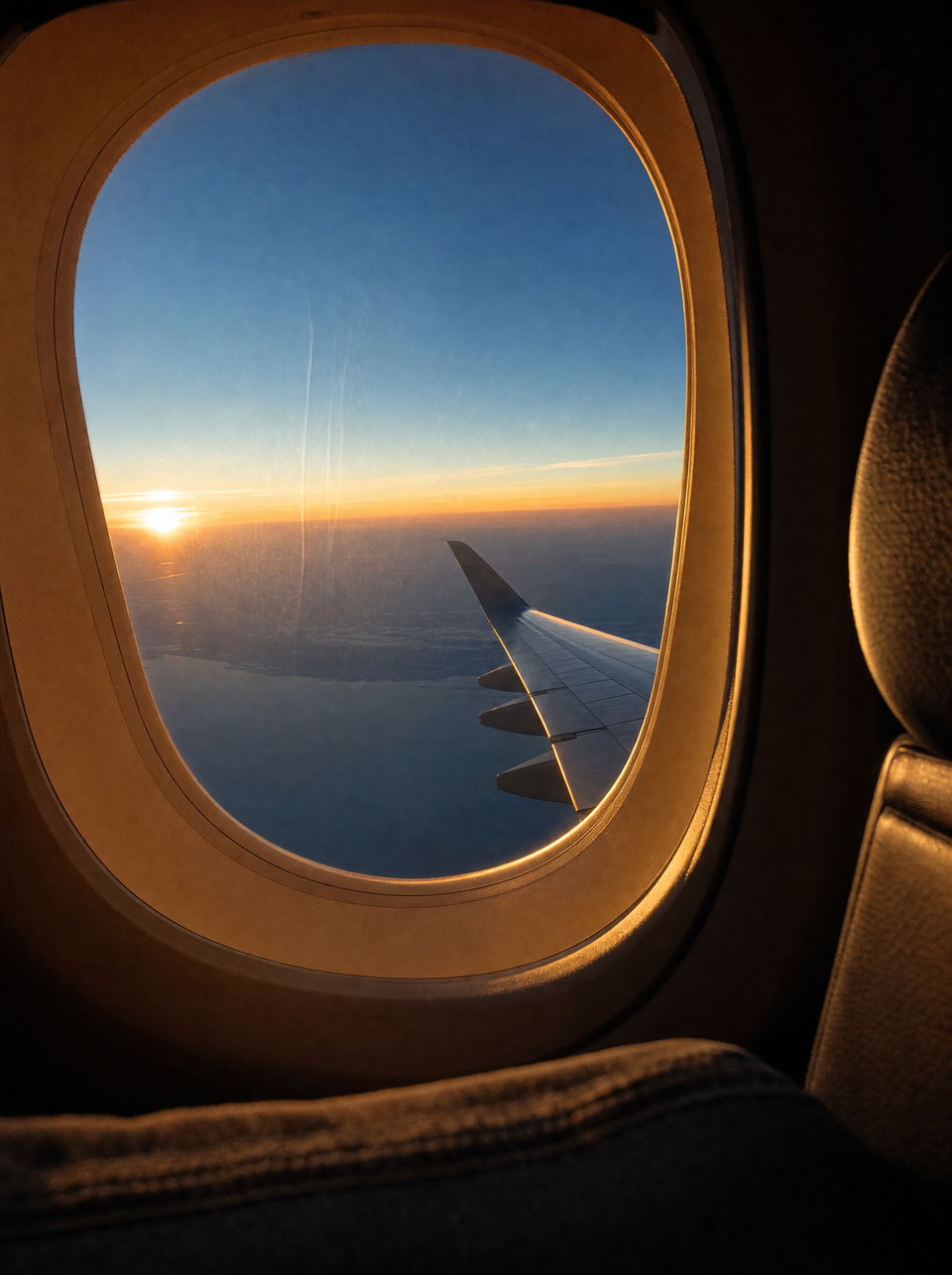 Vista da janela de um avião no fim da tarde, com a asa recortada contra o horizonte.